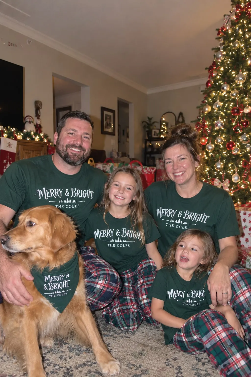 A family and their golden retriever by the Christmas tree in green “Merry & Bright, The Coles” shirts