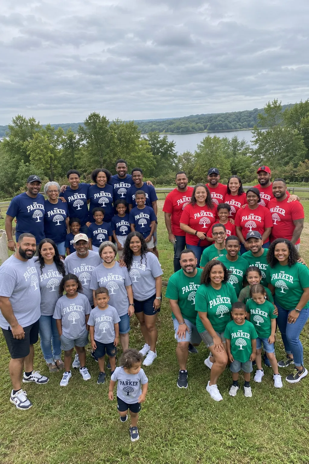 A large family on a hillside in four groups wearing navy, red, grey and green “The Parker Family” tree shirts