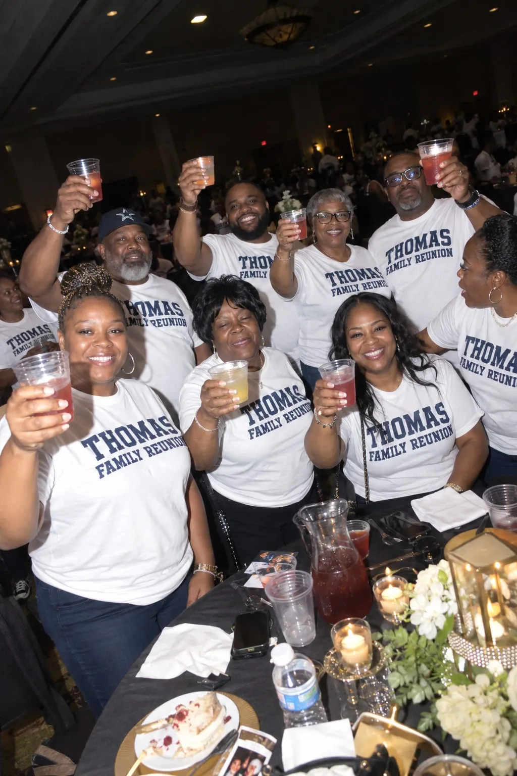 Relatives raising cups at a reunion banquet in matching white shirts reading “Thomas Family Reunion”