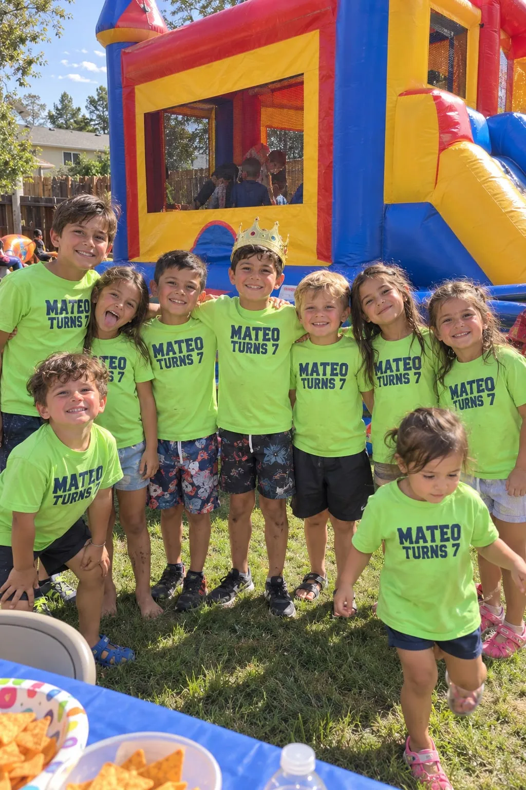 Eight young cousins in front of a bounce house in bright green “Mateo Turns 7” shirts, the birthday boy in a paper crown