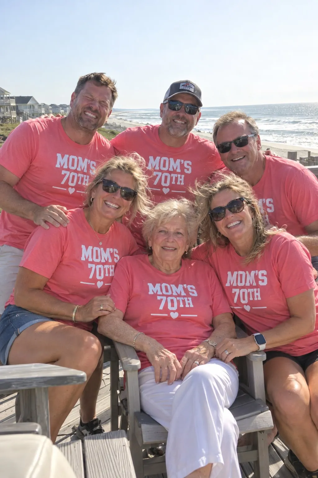 A mother in her seventies with her grown children on a beach house deck, all in pink “Mom’s 70th” shirts