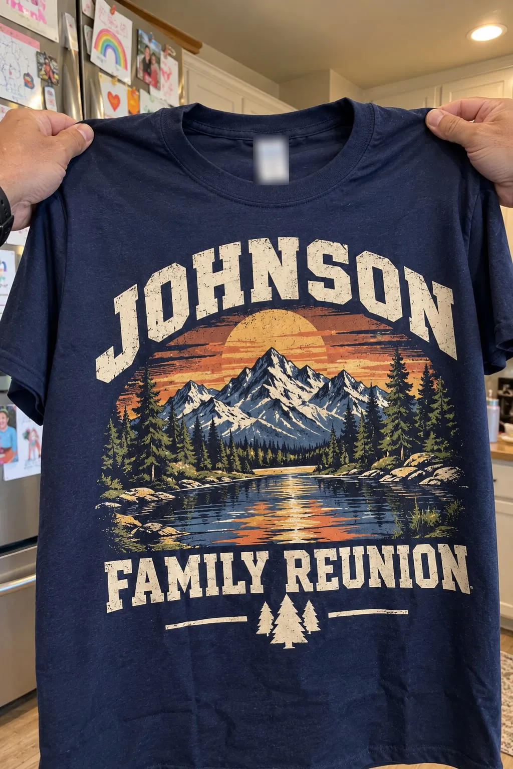 A navy shirt held up in a kitchen with a vintage mountain-and-lake sunset design and “Johnson Family Reunion”